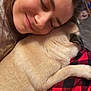 person, dog, snuggling, close_up, cozy, blanket, red_and_black, checkered, fur, sleeping, affection, warmth, indoor, face, smile, comfort, pet, animal, love, relaxation