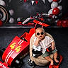 baby, balloons, beanbag, black, checkered_flags, child, cute, decor, floor, helmet, indoor, playful, portrait, racing, red, smiling, sunglasses, toy_car, toy_motorcycle, white