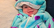 Cassius is registered to the contest to win money with this photo: baby, blanket, child, costume, couch, cute, eyes, fabric, hand, hood, indoor, monster, onesie, pillow, plush, portrait, purple, smiling, turquoise, zipper