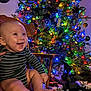 Rowan is registered to the contest to win money with this photo: baby, child, smiling, chair, striped_clothing, christmas_tree, christmas_lights, ornaments, presents, holiday, festive, decorations, indoors, wooden_chair, happy, cute, infant, feet, hands, celebration