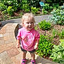 Gemma is registered to the contest to win money with this photo: blonde_hair, casual_clothing, child, daylight, garden, greenery, happy, nature, outdoor, pink_shirt, plants, puma, shrubs, smiling, sneakers, standing, stone_pathway, sunlight, toddler, young_child