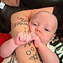 baby, infant, tattoo, arm, couch, clothing, hand, face, person, skin, sleeve, sitting, closeup, indoor, cute, expression, holding, relaxation, comfort, young