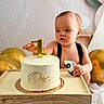 baby, child, birthday, cake, candle, toy_car, golden_balloon, white_frosting, table, wooden_tray, celebration, first_birthday, cute, indoor, portrait, one_year_old, curious, small_hands, party, decor