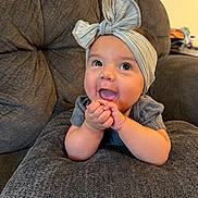 Mariah joined the competition — help win amazing prizes! baby, child, infant, portrait, smiling, happy, tongue_out, bow_headband, headband, hands, sitting, chair, armchair, furniture, indoor, home, gray, close_up, cute, facial_expression