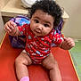 baby, child, infant, red_onesie, pink_socks, curly_hair, orange_mat, backpack, indoor, floor_tiles, baby_gear, cute, chubby, sitting, reaching, portrait, young_child, playful, person, clothing