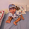 Ricardo Jasiel is registered to the contest to win money with this photo: toddler, child, cap, shirt, bed, pillow, blanket, embroidery, blue, sitting, indoors, cute, looking_up, fabric, smiling, person, clothing, home, furniture, young_child