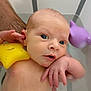 baby, infant, bath, water, toy, yellow_star, purple_dolphin, hand, arm, skin, face, eyes, mouth, person, child, bathroom, playful, cute, floating, support