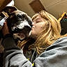 Oreo joined the competition — help win amazing prizes! dog, person, indoor, kiss, affection, casual_clothing, brown_hair, black_dog, close_up, warm_light, hand, love, pet, face, portrait, animal, human, emotion, bond, cozy