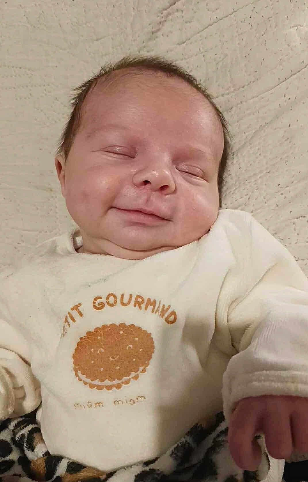 Maylan participe au concours pour gagner de l'argent avec cette photo : baby, infant, sleeping, smile, face, clothing, white_outfit, cute, cozy, blanket, texture, hand, peaceful, child, portrait, indoors, soft_light, newborn, relaxed, expression
