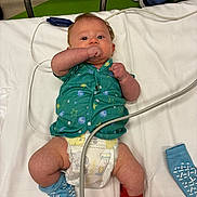 Waylon is registered to the contest to win money with this photo: baby, infant, hospital, medical, bed, diaper, sock, cuff, cable, green_shirt, blue_sock, red_cuff, lying_down, person, healthcare, newborn, cute, indoors, medicine, patient