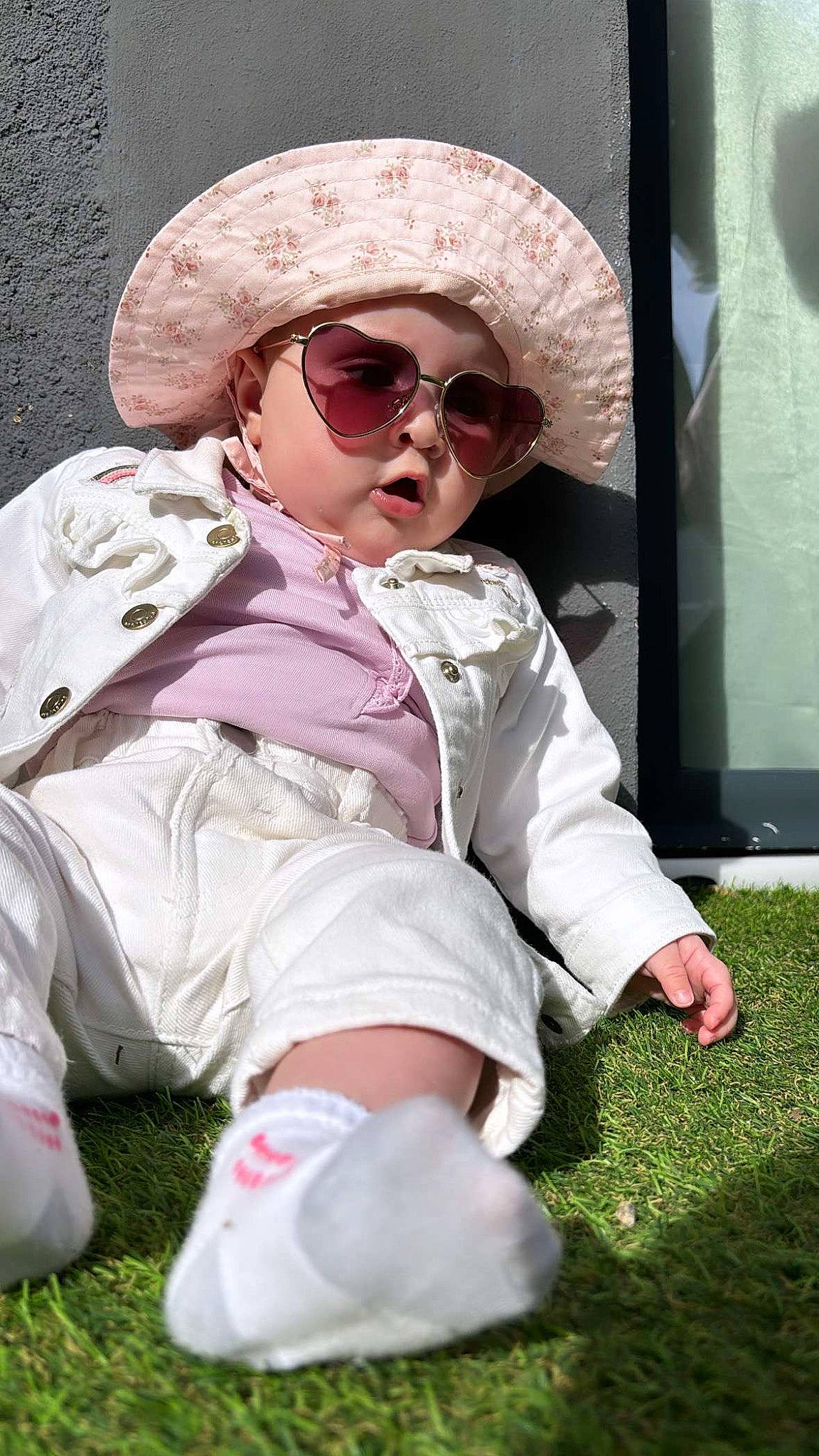 Layana a rejoint le concours — aidez-le/la à gagner de superbes lots ! baby_toddler_clothing, cap, child, eyewear, glasses, goggles, grass, hat, headgear, headwear, human_leg, magenta, person, pink, sitting, sleeve, sneakers, sun_hat, sunglasses, thigh