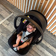 Yzac participe au concours pour gagner de l'argent avec cette photo : baby, car_seat, infant, child, hat, flooring, wooden_wall, straps, black, gray_floor, indoor, person, baby_clothing, modern, seat, safety, cute, looking_up, floor, headwear