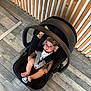 baby, car_seat, infant, child, hat, flooring, wooden_wall, straps, black, gray_floor, indoor, person, baby_clothing, modern, seat, safety, cute, looking_up, floor, headwear