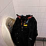 baby_changing_station, backpack, bathroom, black_backpack, compact, corner, cozy, dog, ears, floor_tiles, indoors, peeking, resting, small_dog, stuffed, tile_floor, tiled_wall, unusual_spot, white_tiles, zipper