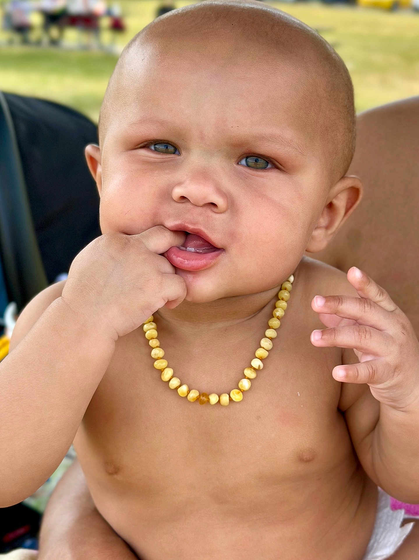 Anthony Jr. joined the competition — help win amazing prizes! baby, child, face, hand, fingers, necklace, beads, skin, outdoor, portrait, curious, expression, closeup, person, infant, chewing, naked_torso, sitting, background_blur, natural_light