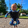 toddler, child, swing, playground, onesie, blue_clothing, smile, happy, outdoor, sunny, trees, grass, woodchips, baby, face, person, daytime, fun, park, seat