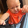 baby, child, orange_shirt, toy_car, steering_wheel, indoor, playtime, cute, face, head, hands, expression, young_child, infant, person, vehicle, fun, smile, play, seat