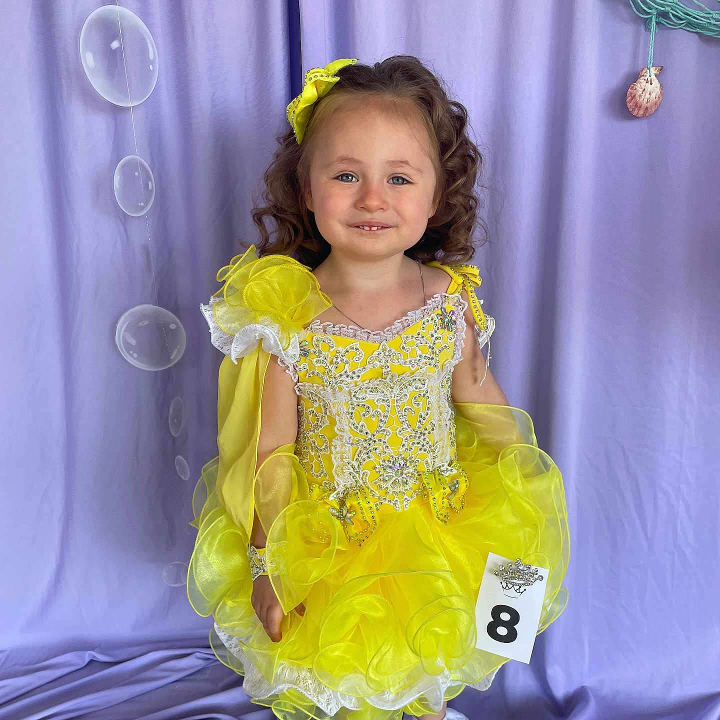 Fenix is registered to the contest to win money with this photo: bow, bubbles, child, childhood, costume, curly_hair, cute, dress_up, fashion, frilly_socks, girl, happy, indoor, pageant, portrait, purple_backdrop, smile, standing, white_shoes, yellow_dress