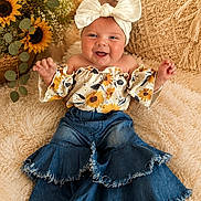 Ruxen is registered to the contest to win money with this photo: baby, child, smiling, headband, bow, sunflower, flower, denim, pants, top, sitting, happy, cute, indoor, cushion, rug, portrait, person, plant, cozy