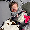 baby, infant, smiling, blanket, stuffed_animal, toy, cushion, fabric, cozy, happy, child, indoor, portrait, cute, clothing, face, hand, soft, playful, comfort