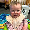 Skyler is registered to the contest to win money with this photo: baby, infant, smiling, pink_clothing, bib, baby_seat, playmat, crib, indoor, child, happy, person, cute, toddler, rosy_cheeks, hands, hair, face, seated, toy