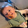 Skyler is registered to the contest to win money with this photo: baby, pacifier, smile, green_bib, infant, happy, lying_down, cute, child, face, skin, clothing, hand, indoors, portrait, young_child, cozy, blanket, warm, closeup