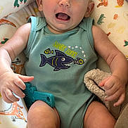 Cohen is registered to the contest to win money with this photo: baby, infant, child, onesie, clothing, shark_design, toy, cushion, seat, smile, happy, skin, arm, leg, hand, face, indoors, colorful, patterned_fabric, comfort