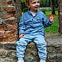 child, boy, smiling, waving, blue_shirt, jeans, white_shoes, stone_wall, brick_pillar, outdoor, garden, greenery, gazebo, casual_clothing, happy, sitting, daylight, portrait, cute, playful