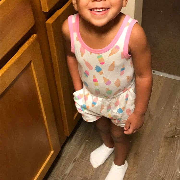 Kamarie is registered to the contest to win money with this photo: bright, casual, child, cute, flooring, glasses, hair_buns, happy, indoors, kitchen, patterned_clothing, person, playful, shorts, smiling, socks, standing, tank_top, wooden_cabinets, young_child