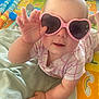 Tamara is registered to the contest to win money with this photo: baby, child, sunglasses, heart_shaped, pink, play_mat, toy, colorful, infant, cute, hand, face, clothing, indoor, person, smiling, young_child, toddler, playful, lying_down