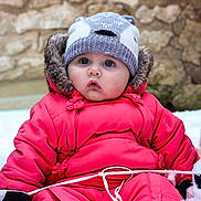 Olivia participe au concours pour gagner de l'argent avec cette photo : baby, infant, bundled_up, pink_snowsuit, knit_hat, fur_trim, blue_eyes, rosy_cheeks, snow, outdoor, stone_wall, mitten, winter_clothing, sitting, rope, cold_weather, portrait, puffy_jacket, cute_expression, hat_with_ears