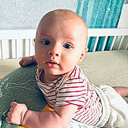 Ambroise a rejoint le concours — aidez-le/la à gagner de superbes lots ! baby, infant, child, striped_shirt, pillow, bedroom, crib, curtains, blue_eyes, cute, expression, furniture, person, laying, soft_lighting, indoor, cushion, white, red, comfort
