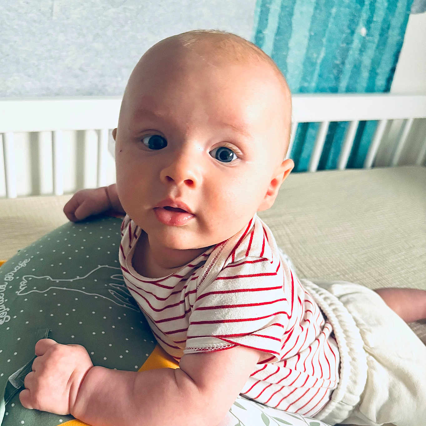 Ambroise a rejoint le concours — aidez-le/la à gagner de superbes lots ! baby, bedroom, blue_eyes, child, comfort, crib, curtains, cushion, cute, expression, furniture, indoor, infant, laying, person, pillow, red, soft_lighting, striped_shirt, white