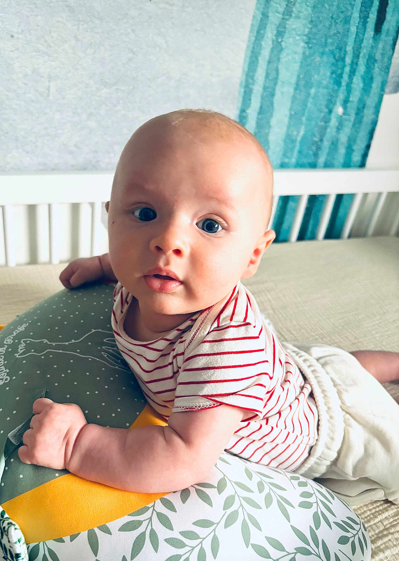 Ambroise a rejoint le concours — aidez-le/la à gagner de superbes lots ! baby, infant, child, striped_shirt, pillow, bedroom, crib, curtains, blue_eyes, cute, expression, furniture, person, laying, soft_lighting, indoor, cushion, white, red, comfort