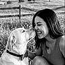 affection, animal_companion, black_and_white, countryside, dog, fence, friendship, grass, hills, labrador, meadow, nose_touch, outdoor, pet, portrait, sitting, smiling, trees, wildflowers, woman