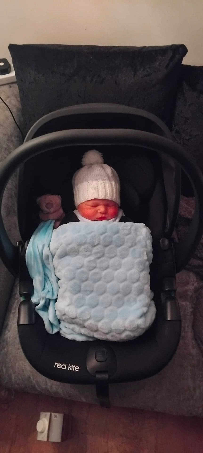 Zach is registered to the contest to win money with this photo: baby, infant, sleeping, car_seat, blanket, knit_hat, teddy_bear, sofa, cushion, indoor, child, person, cozy, soft, plush, resting, newborn, black, blue, pink