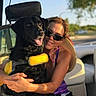 black_dog, boat, boating, dog, facebook_interface, family, hugging, life_jacket, outdoors, person, pet, portrait, smiling, social_media_screenshot, sunglasses, sunlight, tongue_out, vehicle, water, woman