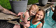 Charley joined the competition — help win amazing prizes! child, toddler, swimming_pool, water, summer, outdoor, sunlight, happy, smiling, tattoo, adult, holding, flower_pot, grass, concrete, swimsuit, wet_hair, family, play, recreation