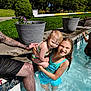 child, toddler, swimming_pool, water, summer, outdoor, sunlight, happy, smiling, tattoo, adult, holding, flower_pot, grass, concrete, swimsuit, wet_hair, family, play, recreation