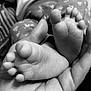 baby_feet, black_and_white, blurred_background, close_up, cute, detail, foot, gentle, hand, human_body, infant, monochrome, newborn, patterned_fabric, resting, skin_texture, small, softness, tender, touch