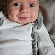 Kayden is registered to the contest to win money with this photo: baby, infant, smiling, face, eyes, dimples, white_clothing, blanket, soft_surface, closeup, cute, child, young, portrait, indoors, happy, lying_down, skin, head, expression