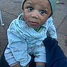 toddler, child, baby, face, eyes, beanie, hat, pajamas, dinosaur_pattern, socks, outdoor, person, hand, clothing, expression, curious, sitting, lap, ground, casual