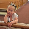 Catalina is registered to the contest to win money with this photo: child, girl, tiara, white_dress, smile, pose, indoor, church, wooden_pews, railing, happy, portrait, braided_hair, jewelry, bracelet, event, celebration, cute, young, fashion