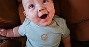 Keith joined the competition — help win amazing prizes! baby, bare_arms, bare_legs, blue_clothing, brown_chair, chair, child, close_up, clothing, eyes, face, happy, home, indoor, infant, laughing, onesie, portrait, sitting, smiling