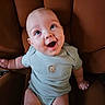 baby, bare_arms, bare_legs, blue_clothing, brown_chair, chair, child, close_up, clothing, eyes, face, happy, home, indoor, infant, laughing, onesie, portrait, sitting, smiling