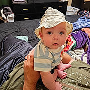 Keith is registered to the contest to win money with this photo: adult_hand, adult_leg, baby, bed, bedroom, blanket, child, clothing, dog, dresser, home, indoor, infant, laundry, photography, portrait, sitting, striped_shirt, sun_hat, wide_eyes
