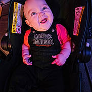 Keith is registered to the contest to win money with this photo: baby, infant, child, smiling, happy, portrait, car_seat, harley_davidson, clothing, black_outfit, pink_sleeves, sitting, indoors, colorful_lighting, close_up, face, hands, automotive, safety_labels, photography