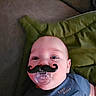 baby, blue_clothing, child, close_up, couch, eyes, face, funny, furniture, green_cushion, indoor, infant, lying_down, mustache, pacifier, photograph, playful, portrait, sitting, smiling
