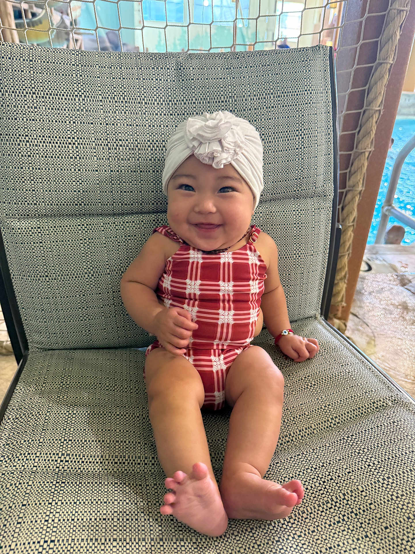 Kissaevynn is registered to the contest to win money with this photo: baby, child, smiling, sitting, swimsuit, turban, flower, chair, patterned_chair, barefoot, indoors, poolside, bracelet, cute, happy, portrait, infant, skin, headwear, plush