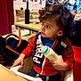 Zeno joined the competition — help win amazing prizes! toddler, child, high_chair, bottle, milk, curly_hair, red_jacket, blue_shirt, restaurant, table, glass, chair, wall_art, people, indoor, food_drink, baby, person, casual, dining